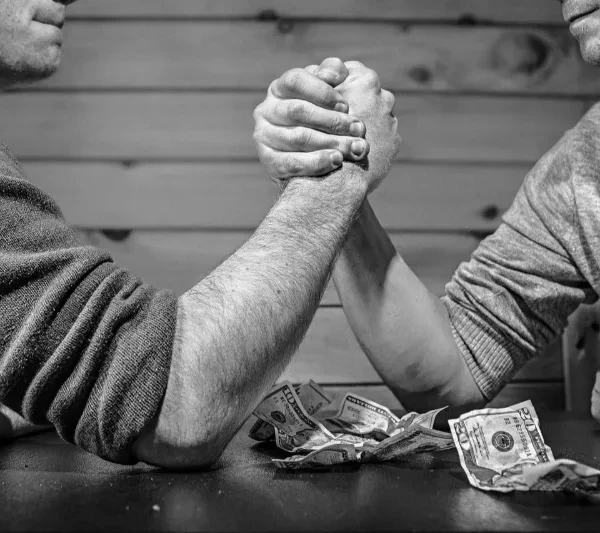 Deux hommes en bras de fer avec billets sur la table, symbolisant l’importance du coût d’une séance d’hypnose ericksonienne.