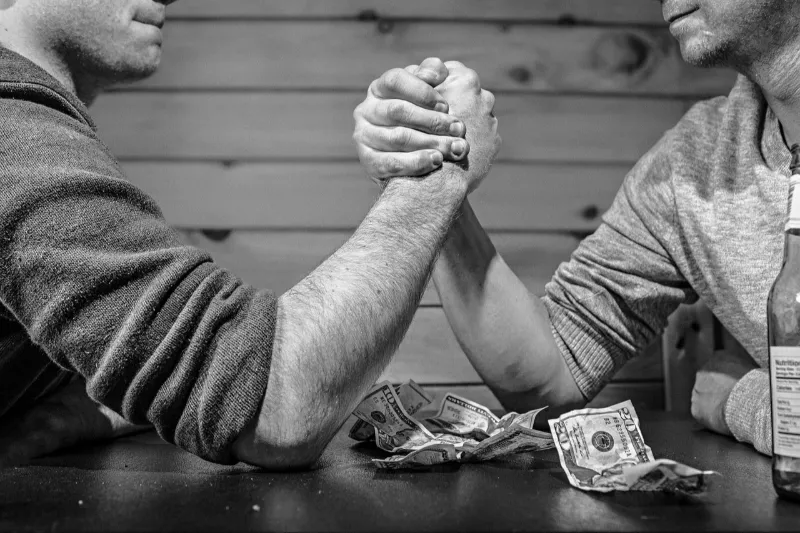 Deux hommes en bras de fer avec billets sur la table, symbolisant l’importance du coût d’une séance d’hypnose ericksonienne.